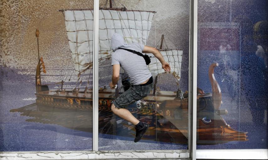 Un manifestante se lanza contra el cristal de un escaparate que muestra una imagen de una antigua galera griega, durante las protestas contra las medidas de austeridad (28 de junio 2011) REUTERS / Yorgos Karahalis