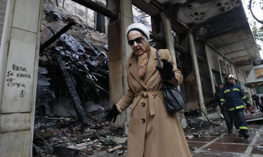 Una mujer pasa junto a un comercio quemado tras los incidentes ocurridos durante la noche que siguió a la aprobación del Parlamento griego de un paquete de medidas de ajuste (13 de febrero 2012). REUTERS / John Kolesidis