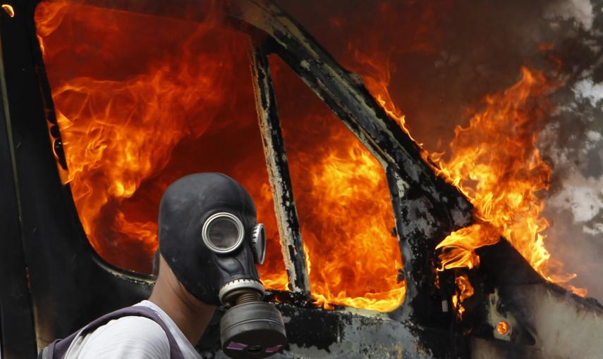 Un manifestante con máscara antigas junto a una furgoneta ardiendo durante las violentas protestas contra las medidas de austeridad en Atenas (28 de junio 2011). REUTERS / Yannis Behrakis