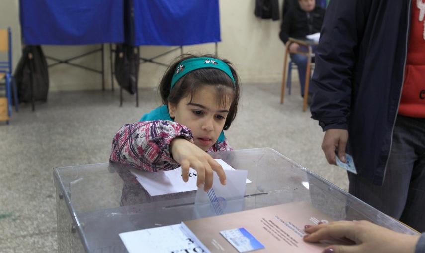 Una niña introduce en la urna el voto de sus padres en un colegio electoral en Atenas. EFE/EPA/SIMELA PANTZARTZI