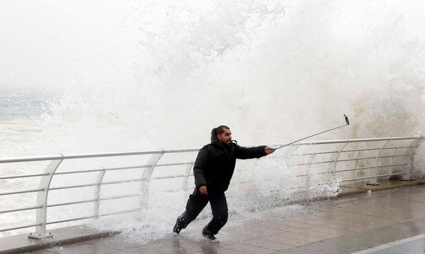 Un hombre se hace un 'selfie' mientas una ola rompe a su espalda, en Líbano. /MOHAMED AZAKIR (REUTERS)