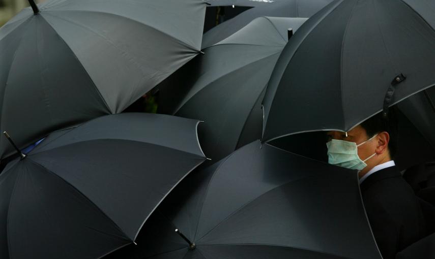 Un hombre con máscara rodeado de paraguas en Hong Kong durante el funeral de un médico víctima del SARS o gripe asiática, que provocó centenares de muertes en China (22 de mayo de  2003). REUTERS / Bobby Yip