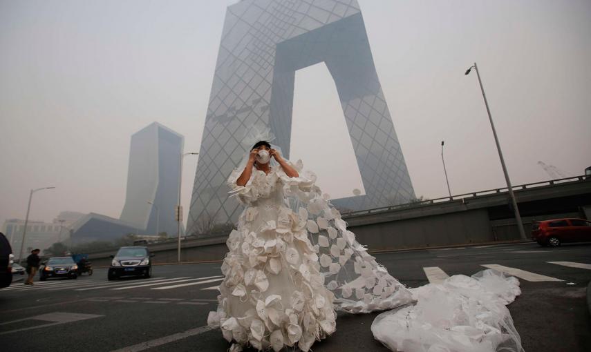 Una mujer posa con un vestido de novia confeccionado con 999 mascarillas para su 'performance' artística 'Cásate con el azul del cielo', ante la sede de la Televisión Central China (CCTV) en un día brumoso en Pekín. /KIM KYUNG-HOON (REUTERS)