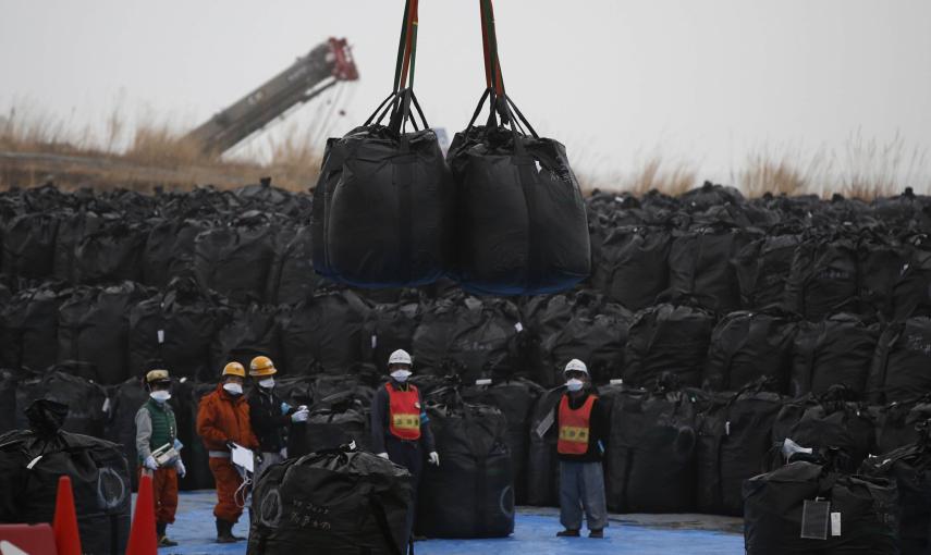 Trabajadores mueven grandes bolsas de plástico que contienen desechos contaminados en un depósito temporal, dentro de la operación de descontaminación de la zona, en la ciudad de Tomioka, provincia de Fukushima./ REUTERS-Toru Hanai