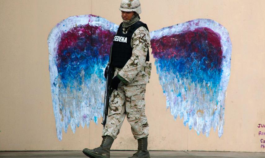 Un soldado camina ante un graffiti que representa las alas de un ángel, realizado por el artista Colette Miller, en Ciudad Juárez (México). /JOSÉ LUIS GONZÁLEZ (REUTERS)