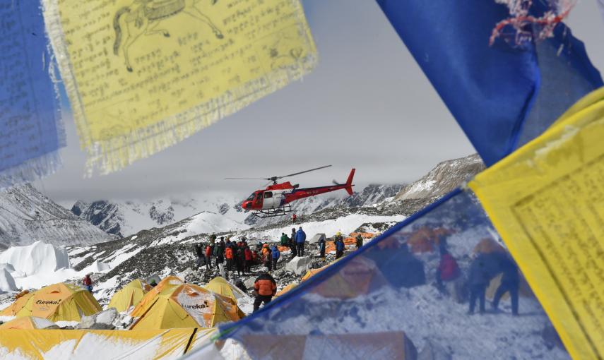 Banderas de oración enmarcan un helicóptero de rescate que transporta a los heridos del campamento base del Everest este domingo.- AFP PHOTO / ROBERTO SCHMIDT