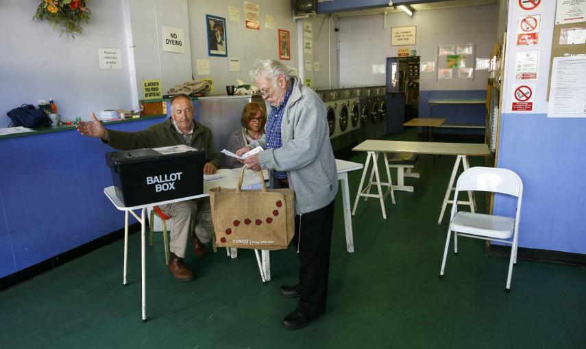 Un hombre recoge su papeleta de voto de las manos de secretarios de colegio en una lavandería pública, que se utiliza como un centro de votación en Oxford./ REUTERS / Eddie Keogh