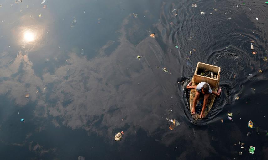 Una mujer rema con las manos en un bote improvisado mientras recoge basura en un río contaminado en la ciudad de Navotas (Filipinas).- ESDRAS ACAYAN (REUTERS)
