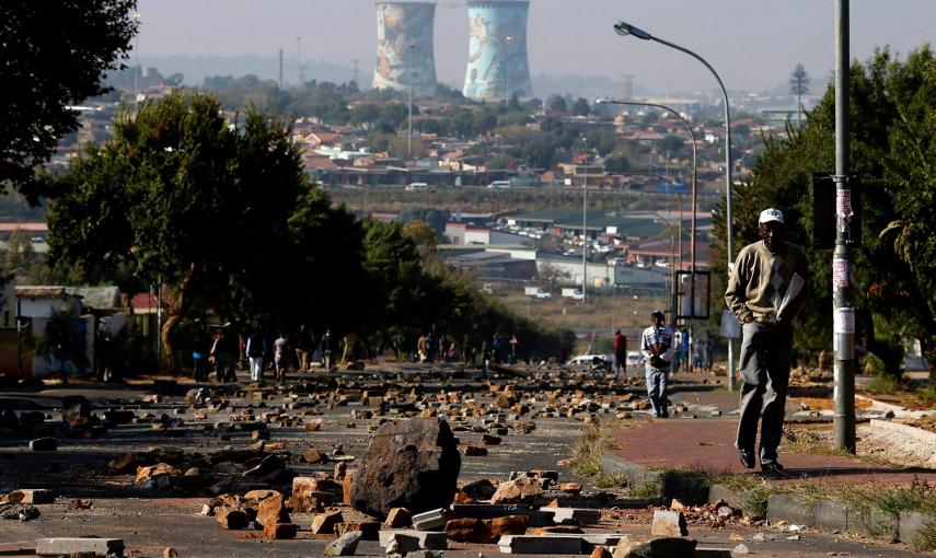 Un hombre camina por una calle llena de rocas y piedras, resultado del enfrentamiento entre manifestantes y policía en Soweto (Suráfrica) por los altos precios de la electricidad.- SIPHIWE SIBEKO (REUTERS)