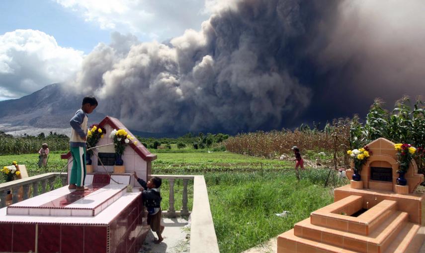 Niños indonesios juegan en un cementerio mientras el monte Sinabung arroja ceniza piroclástica, en Jeraya, Karo./ EFE/ EPA/ DEDI SAHPUTRA