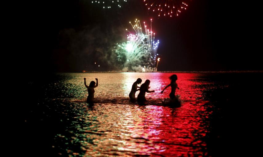 Cuatro mujeres se bañan en el agua mientras a lo lejos, en la Playa de la Misericordia de Málaga, se ven fuegos artificiales para celebrar San Juan./ REUTERS/ Jon Nazca