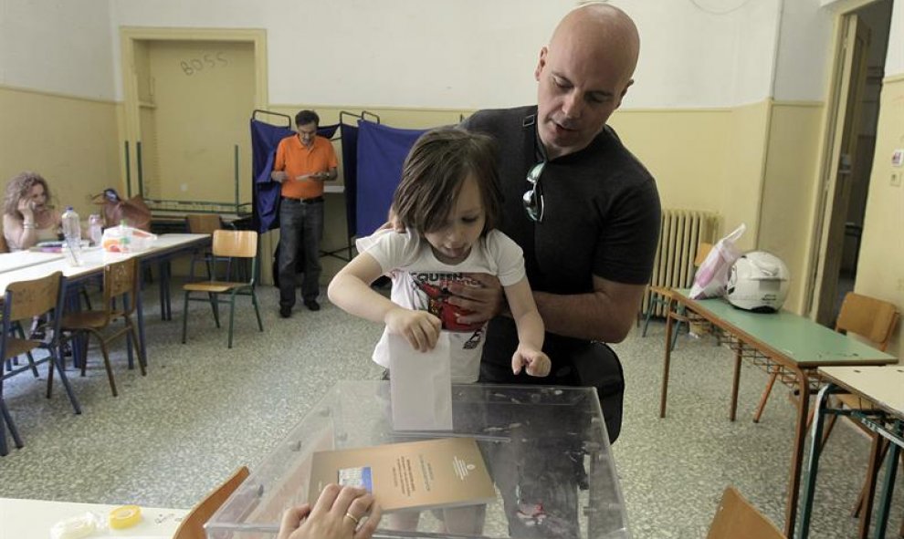 Una niña ayuda a su padre a introducir su voto en la urna en un colegio electoral de Atenas. EFE/EPA/Orestis Panagiotou