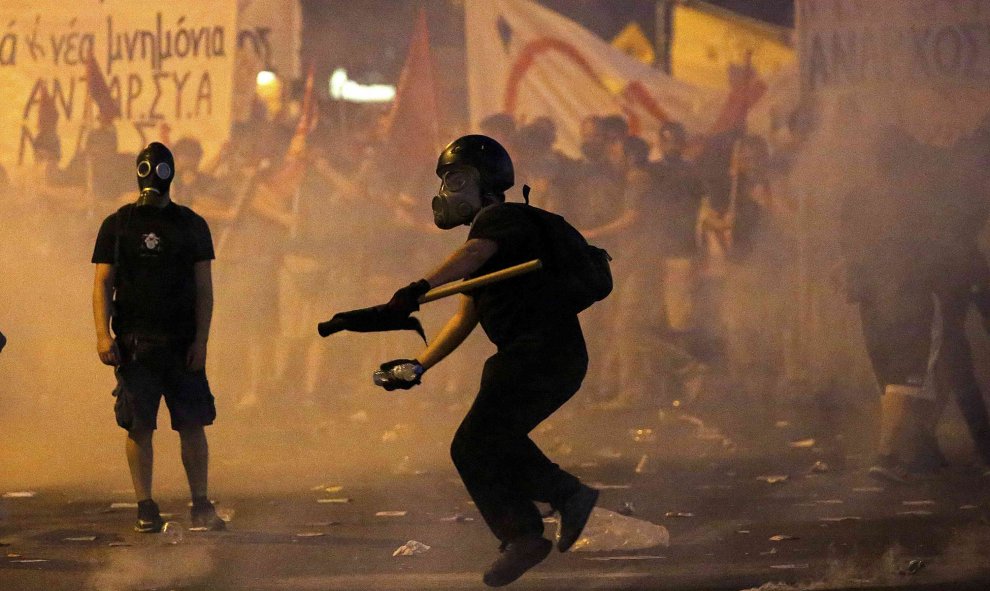 Los manifestantes iban preparados con máscaras antigas. En la imagen, uno de ellos arroja un proyectil incendiario a la policía. EFE/ Yannis Kolesidis