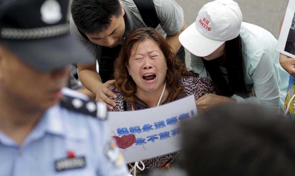 Una mujer cuyo familiar estaba a bordo del vuelo MH370 de Malaysia Airlines, sostiene un cartel que dice : "Mamá estará siempre aquí esperando por ti, nunca te rindas", mientras llora y se arrodilla junto con miembros de la familia ante los medios de comu