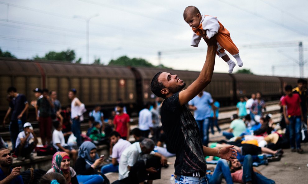 Un inmigrante levanta su bebé mientras espera un tren en dirección a la frontera con Serbia, en la estación de tren en Gevgelija, en la frontera de Macedonia y Grecia el 6 de agosto de 2015.- AFP PHOTO / DIMITAR DILKOFF