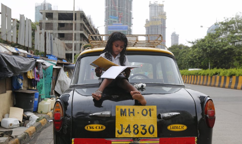 Una niña estudia sentada encima de un taxi al lado de su casa en Bombay./ REUTERS/Shailesh Andrade