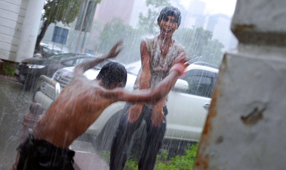 Dos jóvenes indios se divierten jugando bajo un chorro de agua que cae de una fuga en una azotea en el centro de Nueva Delhi, el 11 de agosto de 2015. AFP PHOTO / Roberto SCHMIDT