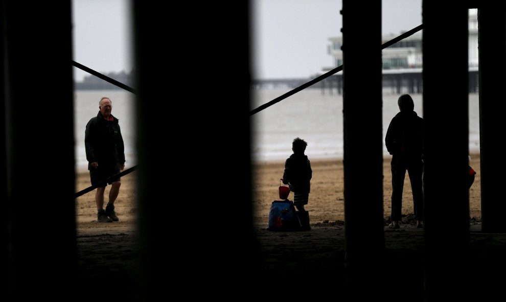 La gente busca refugio de la lluvia debajo de un paseo marítimo en la playa en Weston -super- Mare, en Gran Bretaña. REUTERS