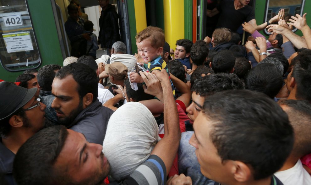 Decenas de refugiados intentan subirse a un vagón de tren entre empujones. /REUTERS