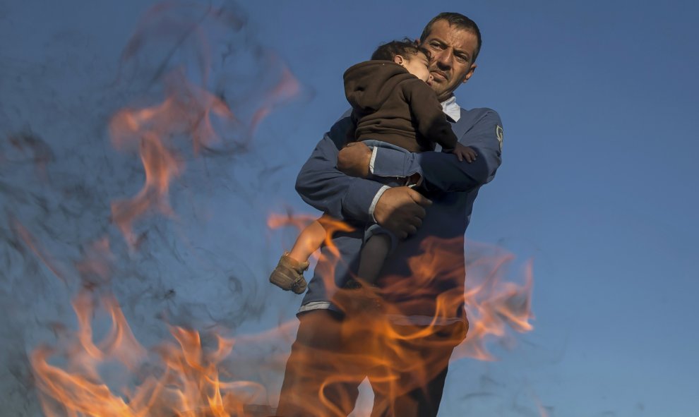 Un inmigrante con su hijo entrando en calor al lado de una fogata en un campamento improvisado en un punto de recogida en el pueblo de Röszke, Hungría, 8 de septiembre de 2015. REUTERS / Marko Djurica