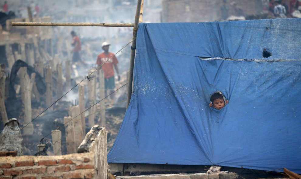 Un niño se asoma por un agujero en una lona en un refugio creado tras un incendio que destruyó cientos de viviendas en la zona Kapuk Raya del norte de Yakarta, 9 de septiembre de 2015. REUTERS / Darren Whiteside