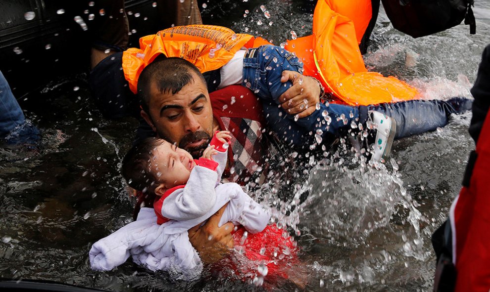 Un refugiado sirio se aferra a sus hijos mientras trata de bajar de su bote en la isla griega de Lesbos, tras cruzar una parte del mar Egeo.- YANNIS BEHRAKIS (REUTERS)