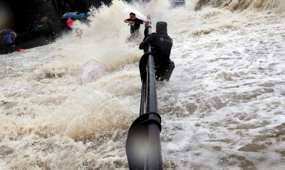 Un policía paramilitar se agarra a una valla mientras turistas intentan escapar de las olas producidas por el tifón Dujuan, en la orilla del río Qiantang, en Hangzhou, provincia de Zhejiang. REUTERS / Stringer,