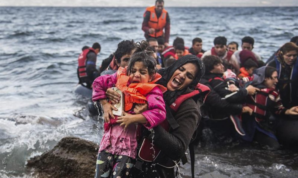 Una refugiada salta de una lancha neumática con su hija en brazos tras alcanzar la costa, en la isla de Lesbos (Grecia). EFE/Filip Singer