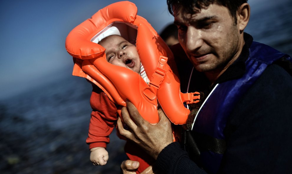 Un emigrante sujeta un bebé mientras refugiados y emigrantes llegan a la isla griega de Lesbos después de cruzar el mar Egeo desde Turquía el 5 de octubre de 2015. AFP / ARIS MESSINIS