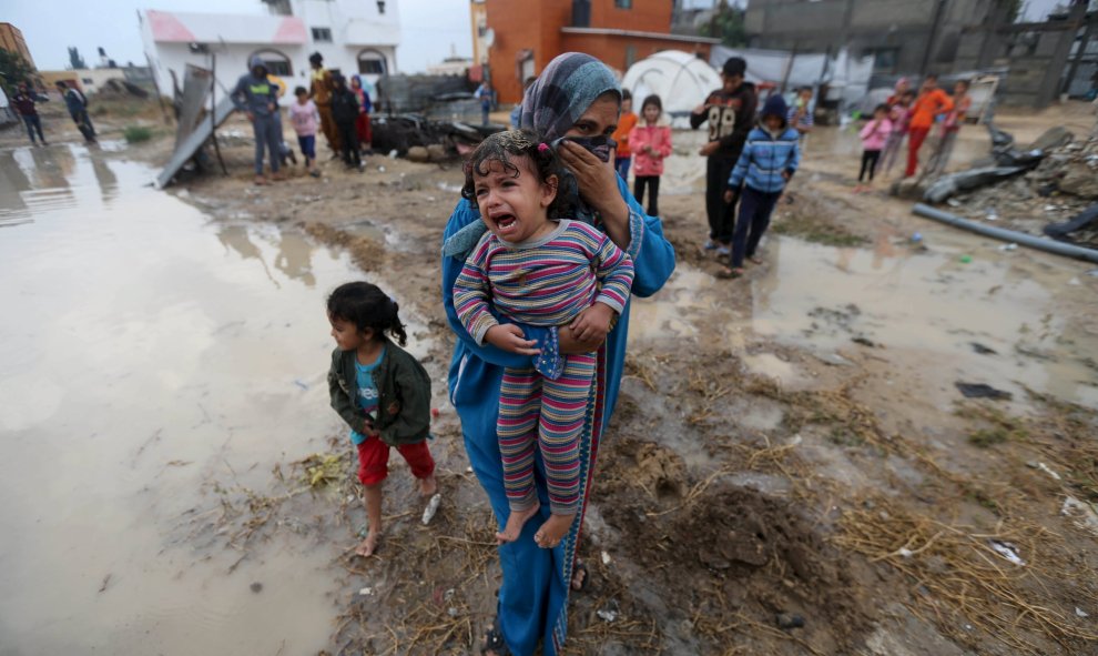 Una mujer palestina lleva a su hija después de que la lluvia inundase su casa que, según testigos, fue dañado por los bombardeos israelíes durante la guerra de 50 días en el verano de 2014, en Khan Younis, en el sur de la Franja de Gaza. REUTERS / Ibrahee