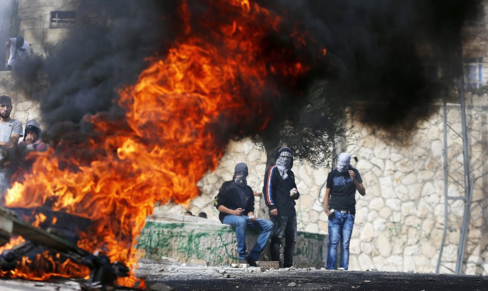 Jóvenes palestinos  lanzando piedras de pie junto a un fuego durante los enfrentamientos con la policía israelí en el este árabe de Jerusalén