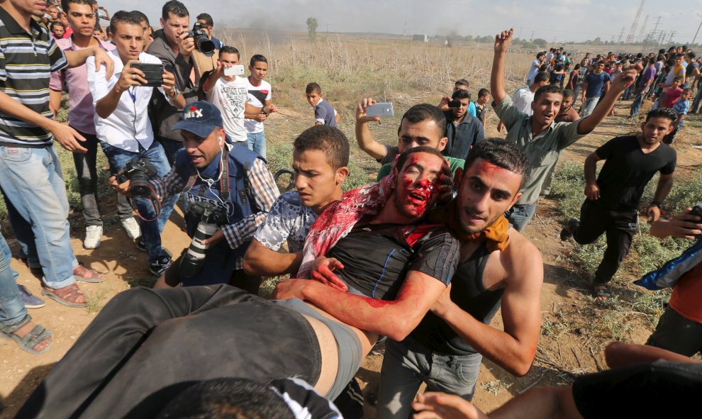 Los palestinos llevan un manifestante herido, fusilado por las tropas israelíes, durante los enfrentamientos cerca de la valla fronteriza israelí en el noreste de la Franja de Gaza. REUTERS/Mohammed Salem