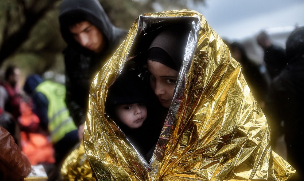 Los niños intentan entrar en calor con mantas de emergencia mientras llegan otros refugiados e inmigrantes a la isla griega de Lesbos. AFP / ARIS MESSINIS