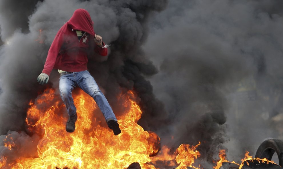 Un manifestante palestino salta sobre varios neumáticos ardiendo durante los enfrentamientos con las tropas israelíes en Bet El, cerca de Ramala. / MOHAMAD TOROKMAN (REUTERS)