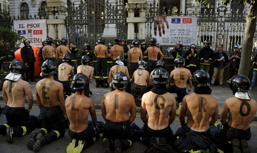 Varios bomberos participan en una protesta frente al parlamento regional de Asturias exigiendo mejores salarios y mayores estándares de seguridad pública en Oviedo, España, 19 de noviembre de 2015. Las letras pintadas sobre las espaldas de los hombres for