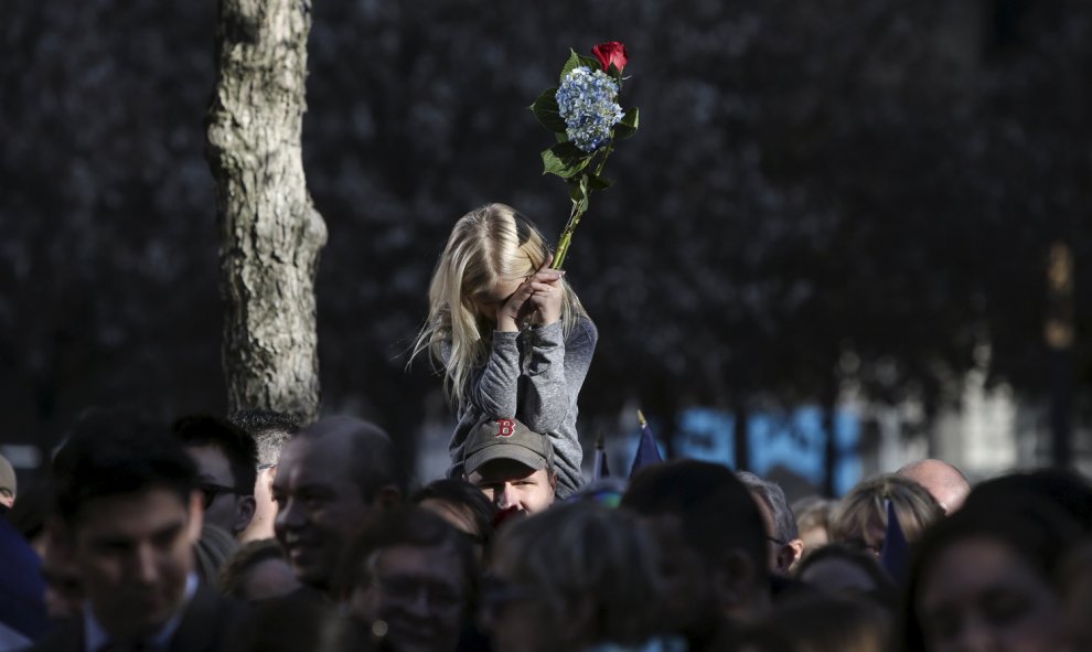 Una niña sostiene un ramo de flores sobre los hombros de sus padre durante un homenaje a las víctimas de los ataques de París en el National Memorial del 11-S de Manhattan, Nueva York.- REUTERS / Andrew Kelly