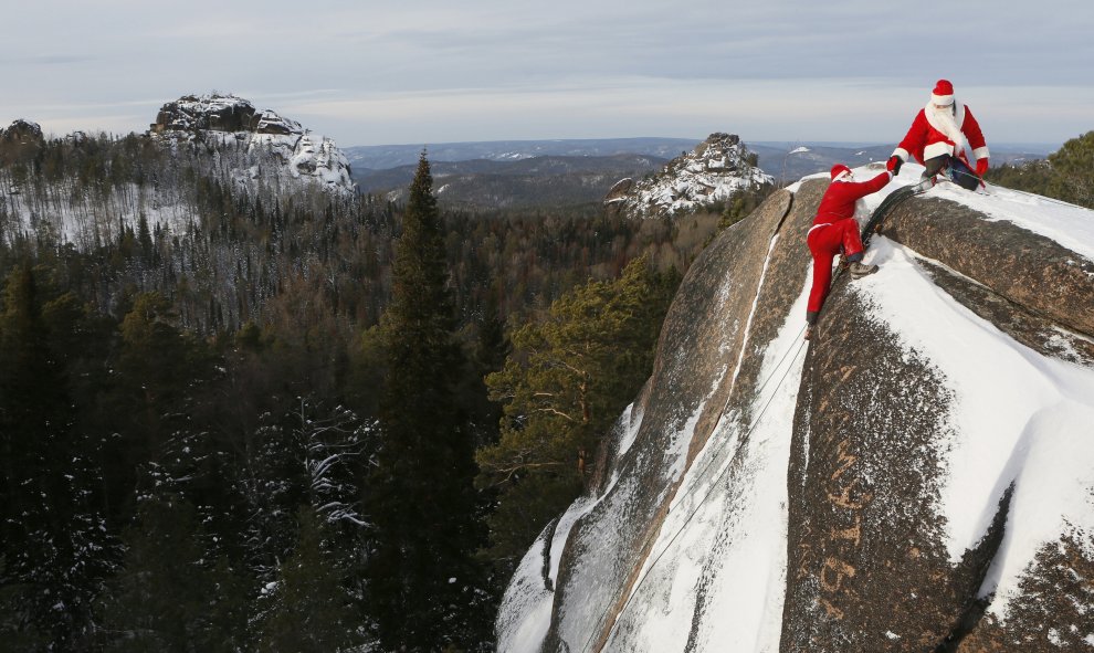 Un miembro de 'Sibspas', grupo de búsqueda y rescate siberiano, vestido de Papá Noel, le a la mano a su compañero que está disfrazado del Padre Invierno, mientras escalan la roca del 'Cuarto Pilar' en la Reserva Nacional de la Naturaleza de Stolby. Krasno