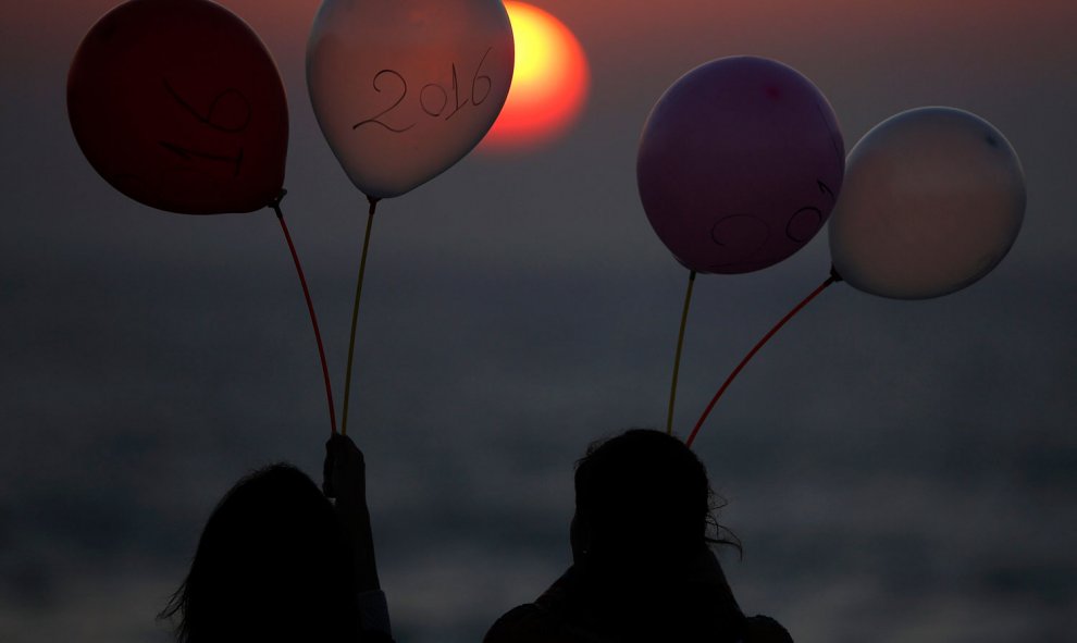 Dos jóvenes palestinas observan el atardecer mientras sostienen globos marcados con el año 2016 hoy, martes 29 de diciembre de 2015, en una playa de la Franja de Gaza. EFE/Mohammed Saber