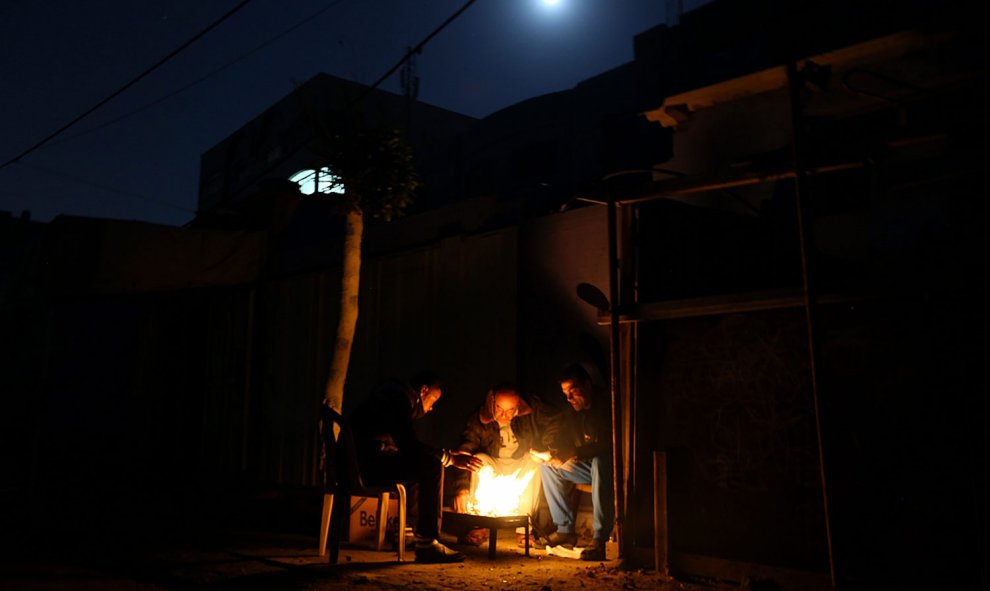 Refugiados palestinos se sientan alrededor de una hoguera durante un corte de luz en el campamento de refugiados de Al Shateaa, cerca de la playa, al oeste de la ciudad de Gaza el 27 de diciembre de 2015. EFE / EPA / MOHAMMED SABER