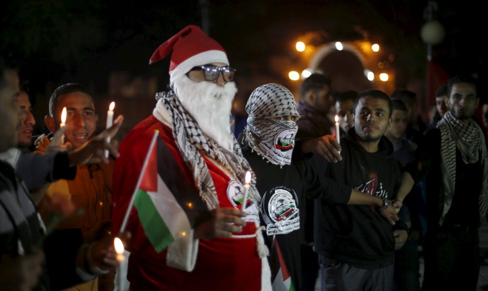 Palestinos enmascarados junto a un hombre  vestido de Papá Noel sostienen velas durante un acto para rendir homenaje a los palestinos asesinados recientemente por las tropas israelíes, el día de Navidad en Gaza.- REUTERS/Suhaib Salem