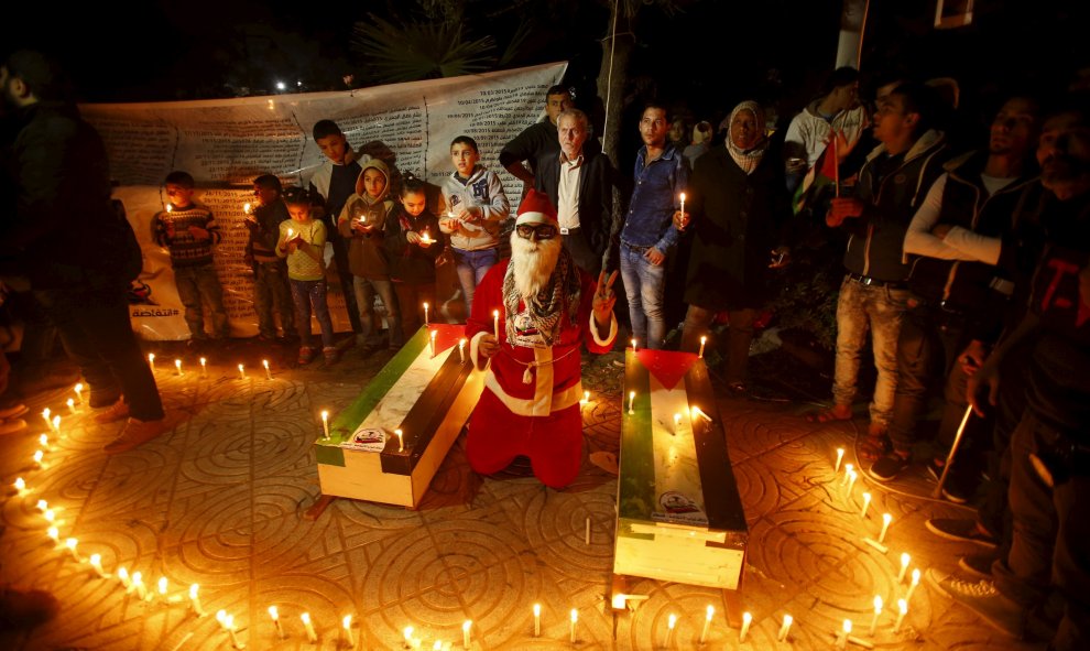 Un hombre vestido de Santa Claus, rodeado de velas, durante un acto para rendir homenaje a los palestinos asesinados recientemente por las tropas israelíes, el día de Navidad en Gaza.- REUTERS/Suhaib Salem