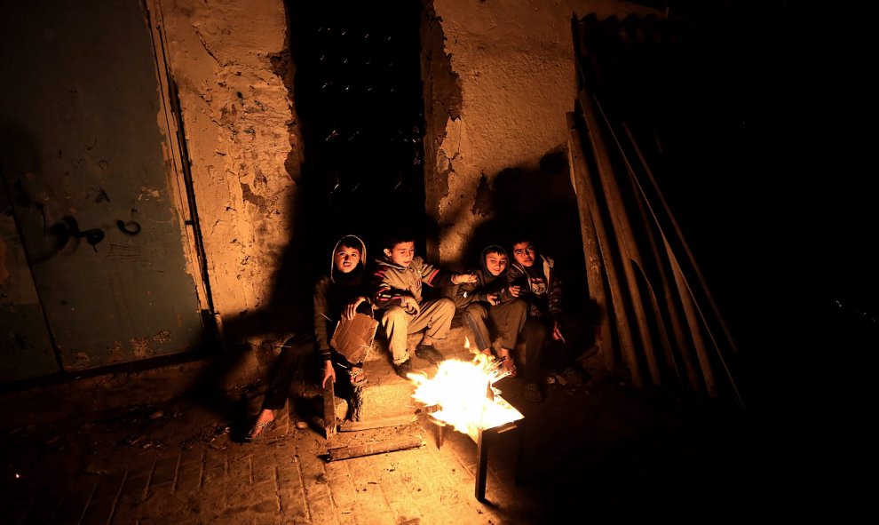 Un grupo de niños refugiados calentándose frente a una fogata luego de un corte de energía en medio del frío en el campamento Al Shateaa en Franja de Gaza. EFE/MOHAMMED SABER