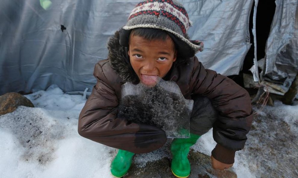 Un niño come un trozo de hielo delante de su refugio temporal en Laprak, en el distrito de Gorkha (Nepal). EFE/Narendra Shrestha