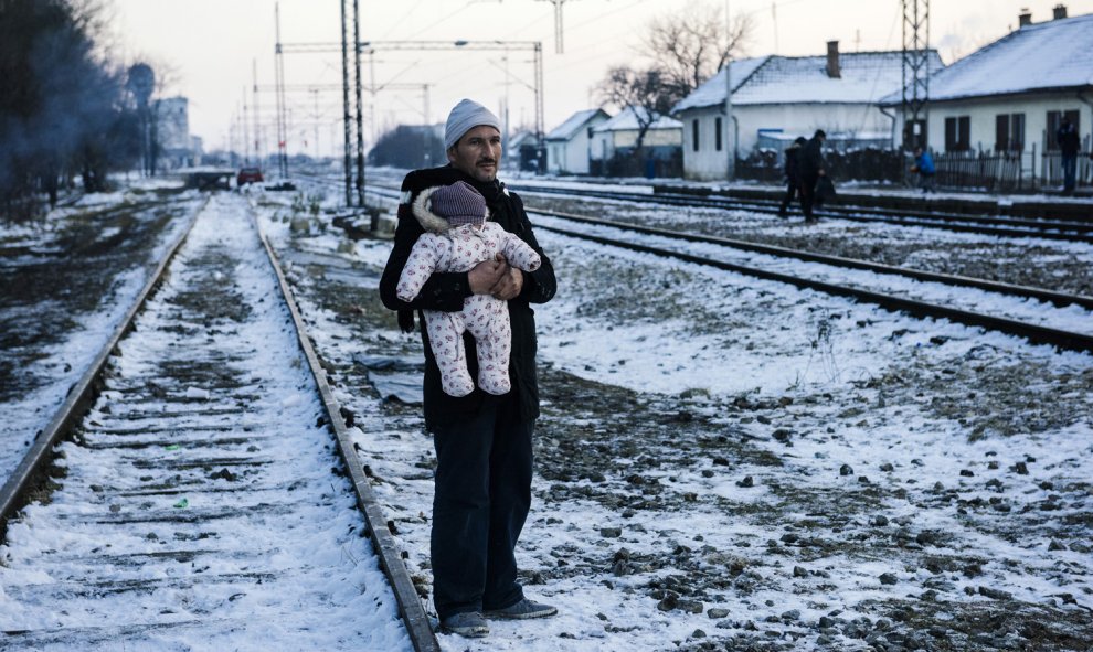 Un hombre sostiene a su bebé mientras espera con otros inmigrantes y refugiados en una estación de tren a un tren en el sur de Presevo en Serbia, 20 de enero 2016./AFP