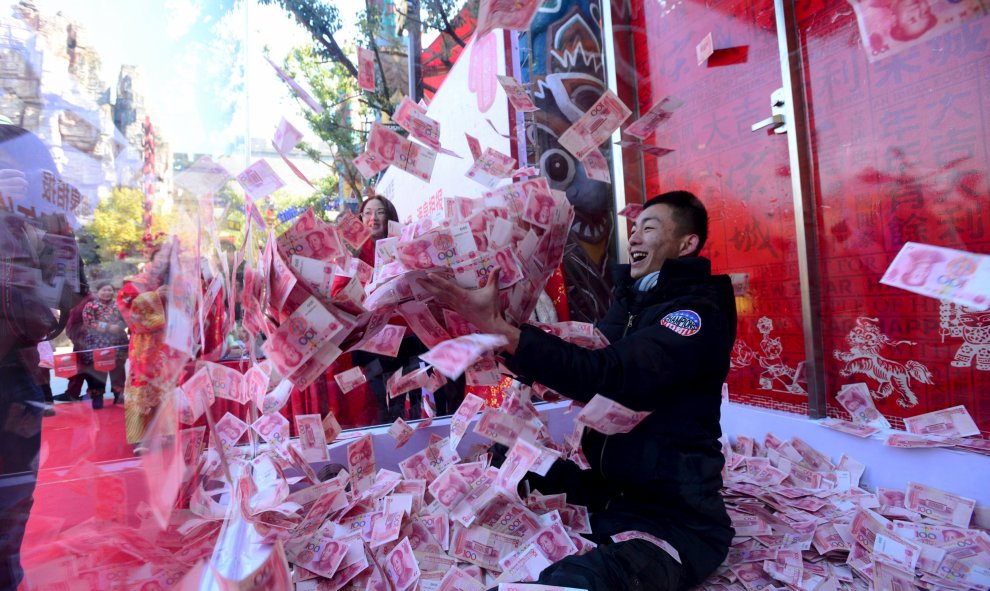 Un hombre intenta sacar billetes de 100 yuanes dentro de una jaula de cristal durante un evento realizado para celebrar el próximo Festival de Primavera, en un parque en Hangzhou, provincia de Zhejiang, China. REUTERS/Stringer