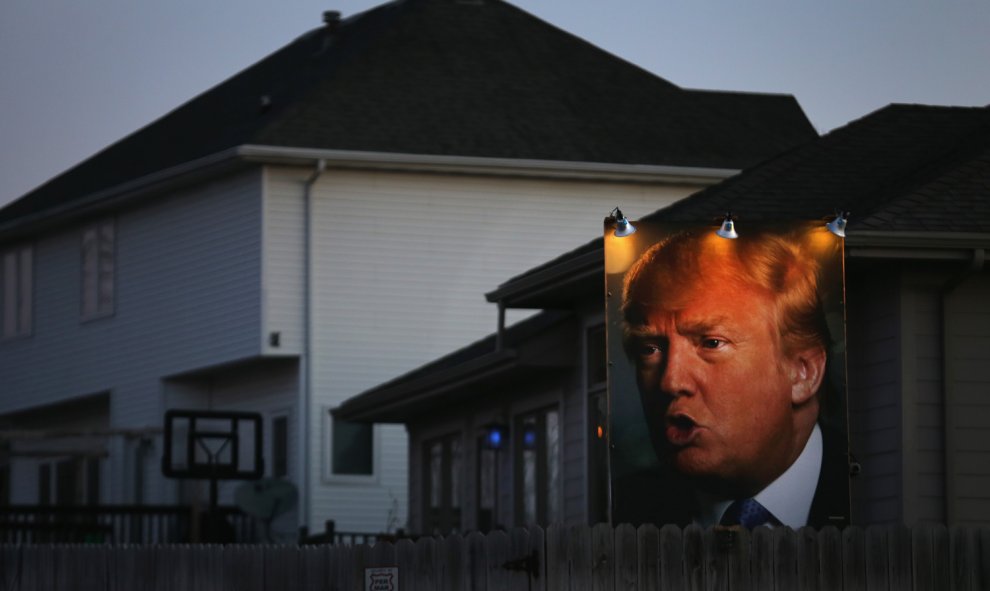Un partidario de Donald Trump coloca un póster gigante del político iluminado con focos en la parte trasera de su casa para mostrar su apoyo al candidato./AFP/Christopher Furlong