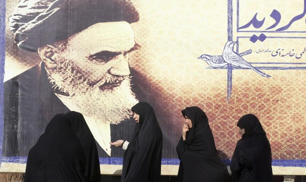 Mujeres iraníes pasan delante de un cartel con la foto del fallecido fundador de la República Islámica de Irán, ayatolá Ruhola Jomeini, en el cementerio de Behesht-e Zahra en Teherán, Irán). Irán celebra hoy el 37 aniversario del regreso de Jomeini a Irán