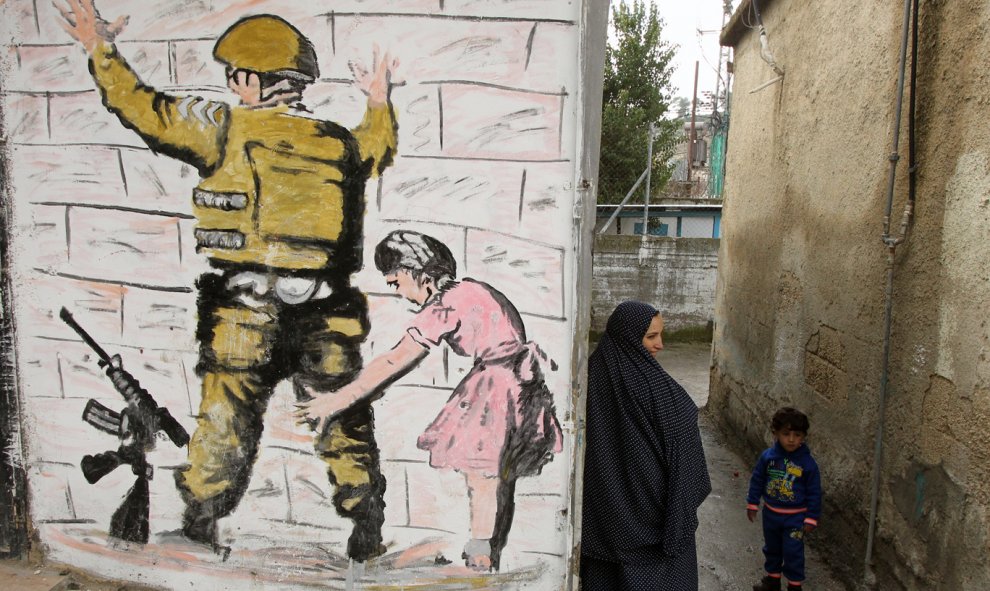 Una mujer palestina se encuentra con un niño en un callejón junto a la reproducción de un mural del artista callejero británico Banksy en al-Aroub campo de refugiados palestinos, al norte de la ciudad cisjordana de Hebrón. HAZEM BADER/AFP