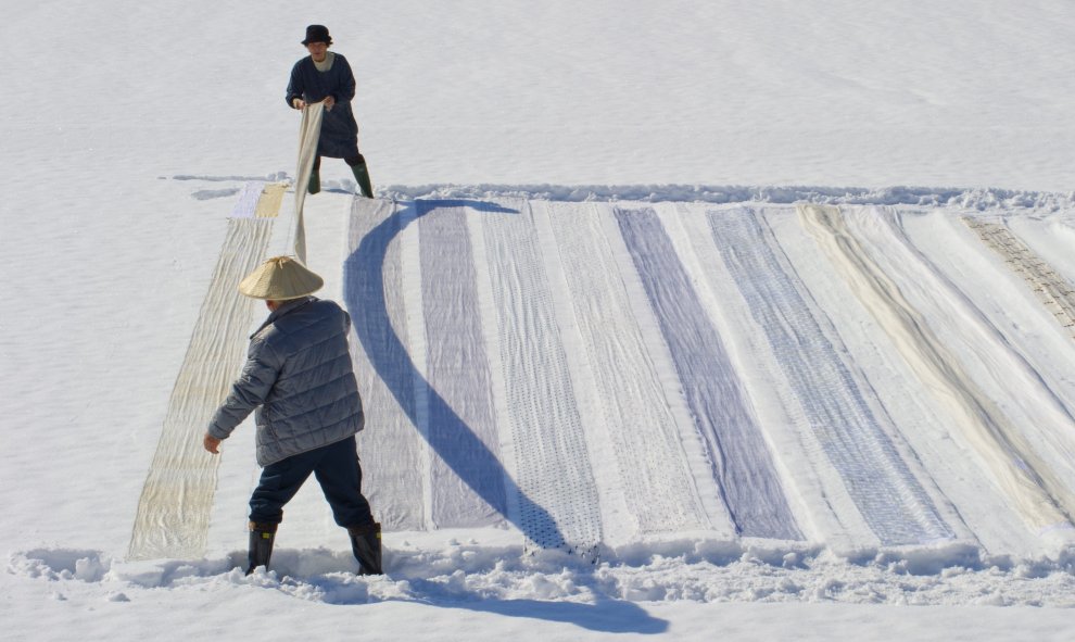 Una pareja coloca tela de kimonos sobre la nieve para su limpieza en Shiozawa en la prefectura de Niigata en Japón. EFE/Everett Kennedy Brown