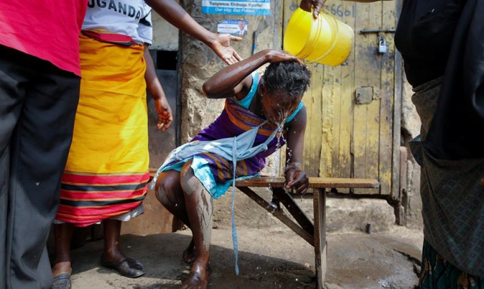 Varias personas ayudan a una mujer que recibió una bomba de gas lacrimógeno, lanzada por policías, cerca de la sede del partido del candidato opositor y principal rival de Yoweri Museveni en las elecciones presidenciales, Kizza Besigye, en Kampala, Uganda